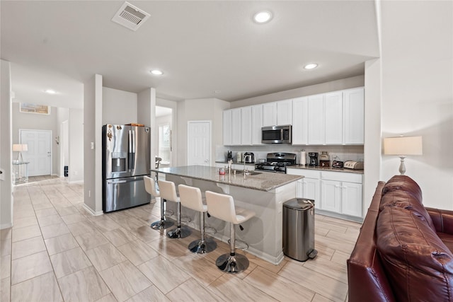 kitchen featuring a breakfast bar, white cabinetry, stone countertops, an island with sink, and stainless steel appliances