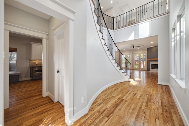 stairway with wood-type flooring, a towering ceiling, and ceiling fan