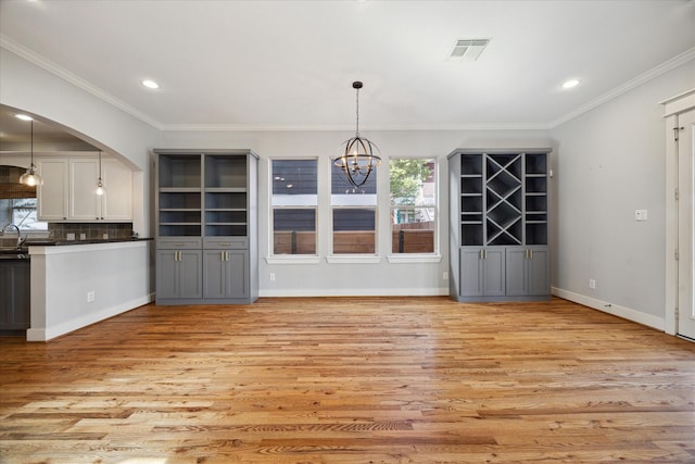 unfurnished dining area with crown molding, sink, light hardwood / wood-style floors, and a notable chandelier