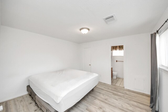 bedroom with ensuite bath and light wood-type flooring