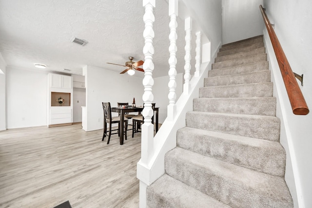 staircase featuring hardwood / wood-style floors, a textured ceiling, and ceiling fan