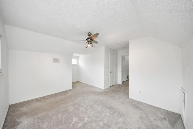 carpeted spare room featuring ceiling fan, vaulted ceiling, and a textured ceiling
