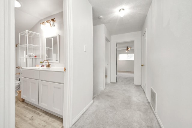 hall with light carpet, sink, and a textured ceiling