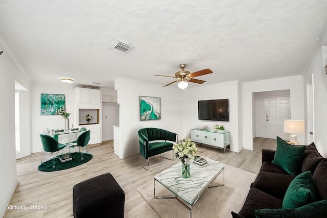 living room featuring ceiling fan, light hardwood / wood-style flooring, and a textured ceiling