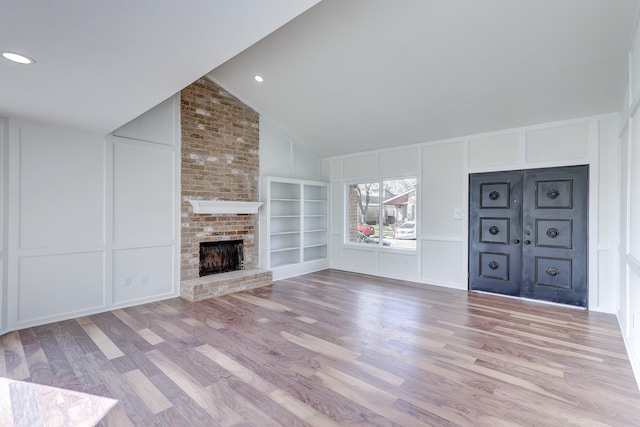 unfurnished living room featuring built in features, a fireplace, vaulted ceiling, and light hardwood / wood-style flooring