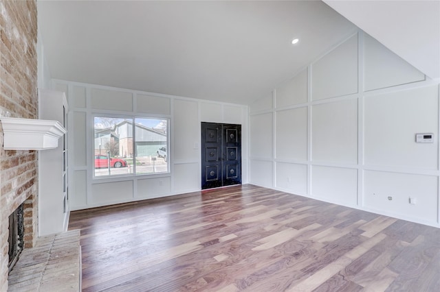 unfurnished living room featuring a brick fireplace, hardwood / wood-style floors, and lofted ceiling