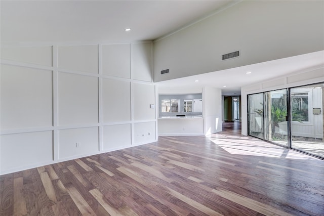 unfurnished living room with high vaulted ceiling, a healthy amount of sunlight, and hardwood / wood-style floors