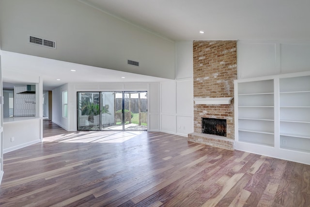 unfurnished living room featuring a brick fireplace, hardwood / wood-style floors, and high vaulted ceiling