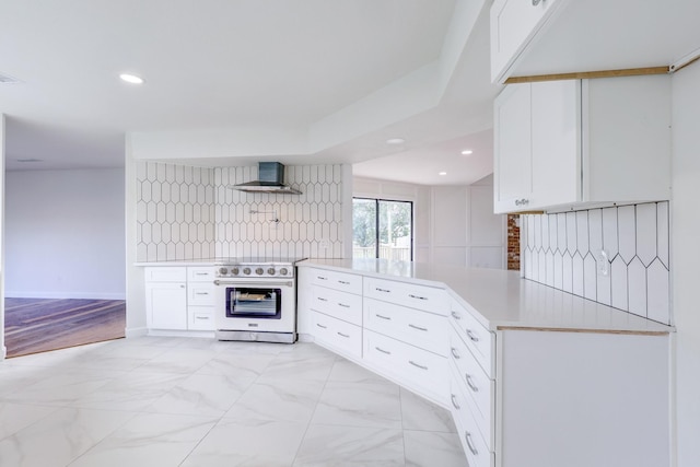 kitchen with white cabinets, wall chimney range hood, high end stainless steel range, and kitchen peninsula