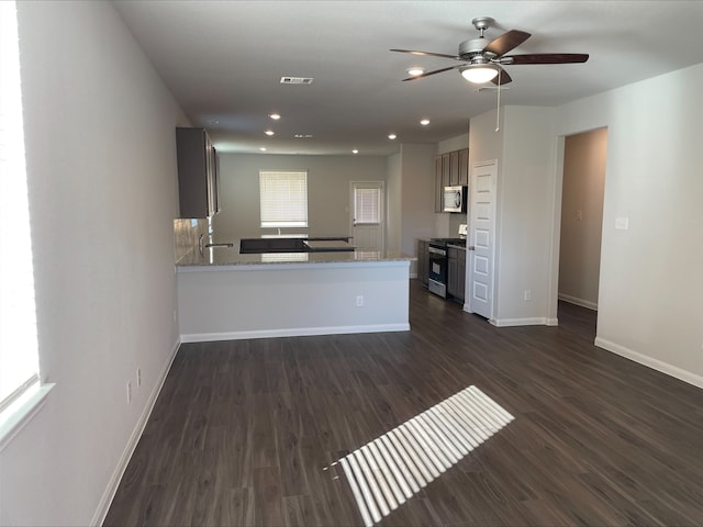 kitchen with appliances with stainless steel finishes, dark hardwood / wood-style floors, ceiling fan, kitchen peninsula, and light stone countertops