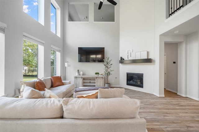 living room featuring a wealth of natural light, a large fireplace, ceiling fan, and light wood-type flooring