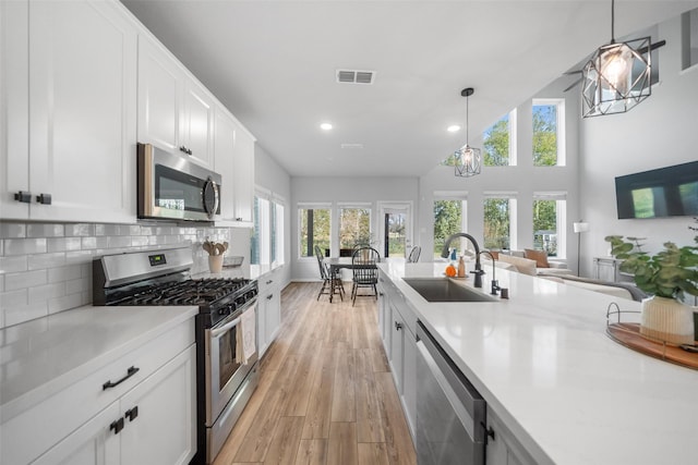 kitchen with decorative light fixtures, white cabinetry, sink, backsplash, and stainless steel appliances