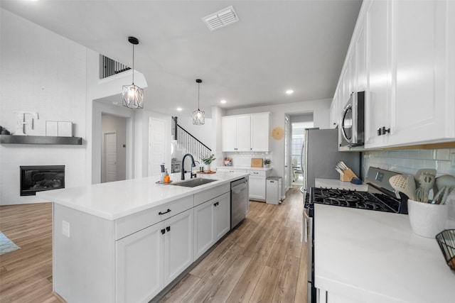 kitchen with decorative light fixtures, white cabinetry, sink, a kitchen island with sink, and stainless steel appliances