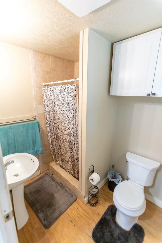 bathroom with wood-type flooring, toilet, a textured ceiling, and walk in shower