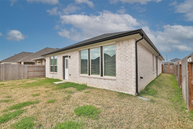 back of house featuring brick siding, a lawn, and a fenced backyard