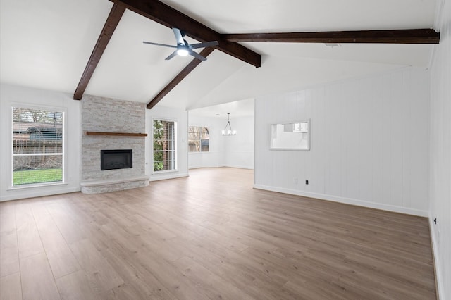 unfurnished living room with hardwood / wood-style flooring, a stone fireplace, lofted ceiling with beams, and ceiling fan with notable chandelier