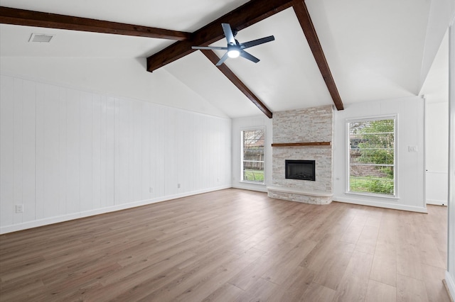 unfurnished living room featuring ceiling fan, a stone fireplace, light hardwood / wood-style floors, and vaulted ceiling with beams