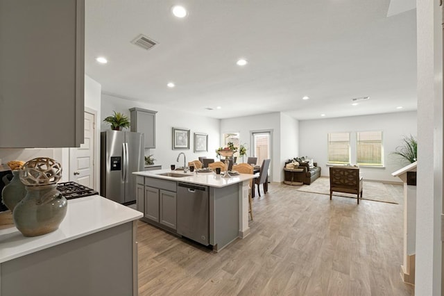 kitchen with sink, a center island with sink, gray cabinets, and appliances with stainless steel finishes