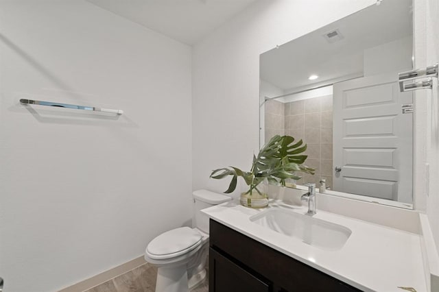 bathroom featuring vanity, wood-type flooring, tiled shower, and toilet