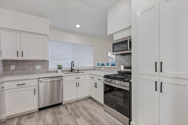 kitchen with appliances with stainless steel finishes, white cabinetry, sink, decorative backsplash, and light hardwood / wood-style flooring