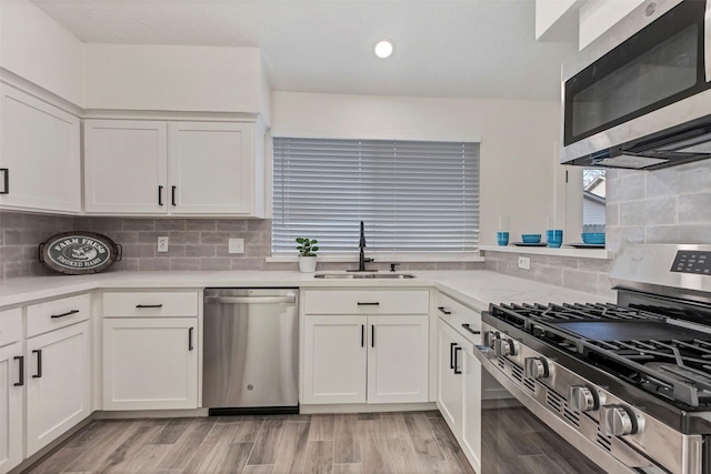 kitchen with sink, light wood-type flooring, appliances with stainless steel finishes, white cabinets, and backsplash