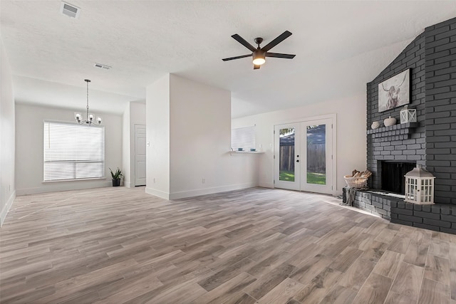 living room with french doors, ceiling fan with notable chandelier, a brick fireplace, and light wood-type flooring