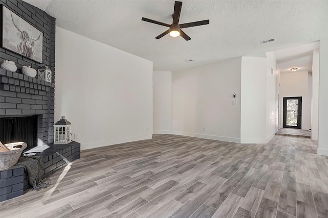 unfurnished living room with ceiling fan, light wood-type flooring, a textured ceiling, and a fireplace