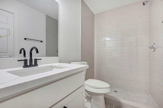 bathroom with vanity, toilet, a textured ceiling, and a tile shower