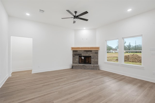 unfurnished living room featuring ceiling fan, a stone fireplace, and light hardwood / wood-style floors