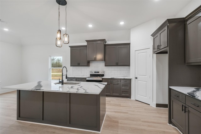 kitchen featuring sink, electric stove, light stone countertops, a kitchen island with sink, and decorative backsplash