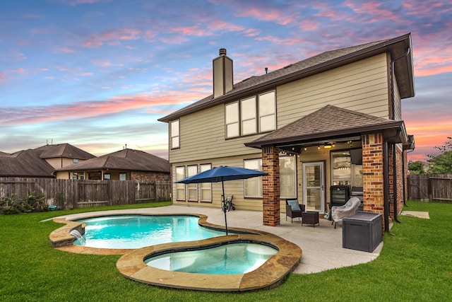 pool at dusk featuring an in ground hot tub, a patio area, and a lawn