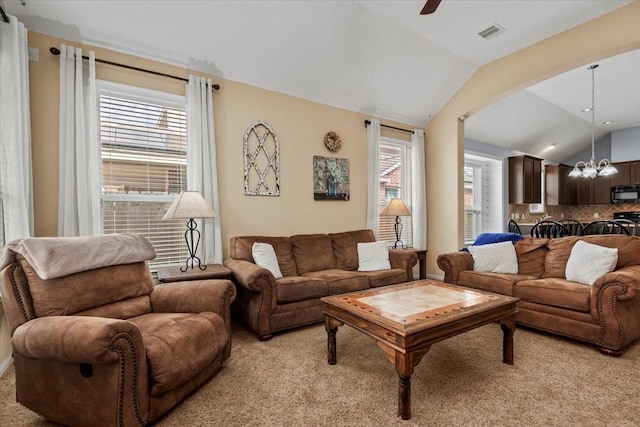 living room with vaulted ceiling, ceiling fan with notable chandelier, a wealth of natural light, and light colored carpet