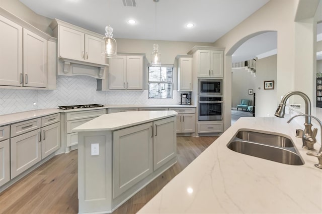 kitchen with sink, hanging light fixtures, light wood-type flooring, stainless steel appliances, and light stone countertops