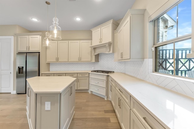 kitchen featuring appliances with stainless steel finishes, backsplash, hanging light fixtures, custom exhaust hood, and light hardwood / wood-style floors