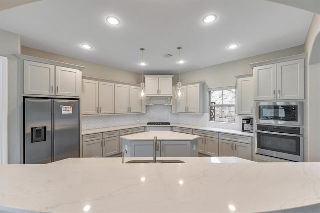 kitchen featuring sink, tasteful backsplash, decorative light fixtures, stainless steel appliances, and light stone countertops