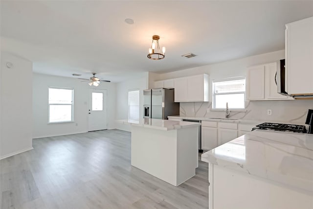 kitchen featuring a kitchen island, appliances with stainless steel finishes, pendant lighting, sink, and light stone countertops