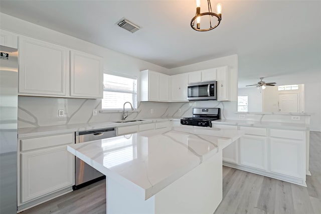 kitchen featuring sink, a center island, hanging light fixtures, appliances with stainless steel finishes, and white cabinets