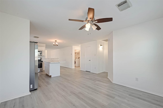 unfurnished living room with ceiling fan, a barn door, washer / clothes dryer, and light hardwood / wood-style flooring