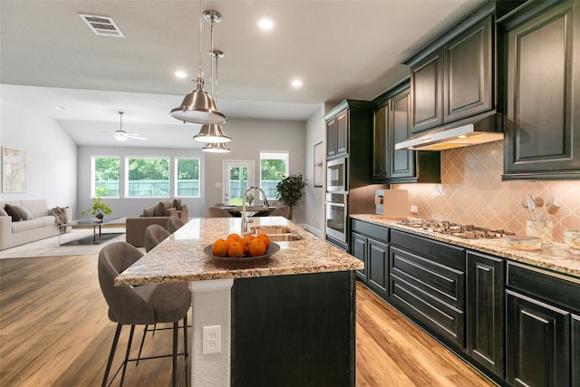 kitchen with appliances with stainless steel finishes, sink, a kitchen bar, a center island with sink, and light hardwood / wood-style flooring