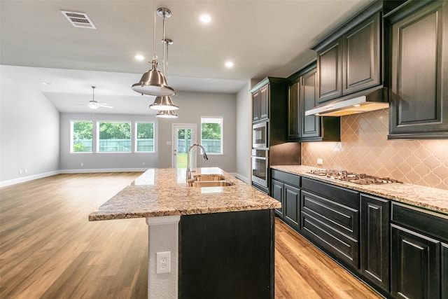 kitchen with stainless steel gas cooktop, sink, decorative light fixtures, light hardwood / wood-style flooring, and a kitchen island with sink