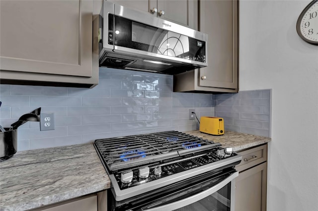 kitchen with tasteful backsplash, gray cabinets, light stone countertops, and range with gas cooktop