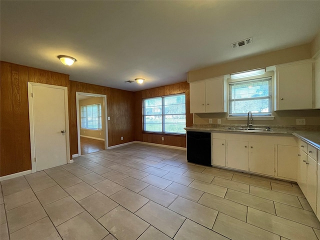 kitchen featuring light tile patterned flooring, wood walls, white cabinetry, dishwasher, and sink