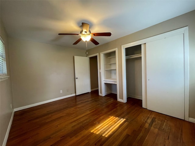 unfurnished bedroom with dark wood-type flooring, ceiling fan, and two closets