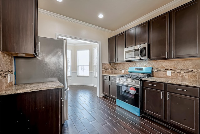 kitchen with appliances with stainless steel finishes, dark brown cabinetry, light stone counters, and ornamental molding