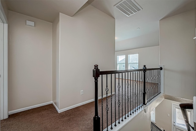 hall with carpet floors, baseboards, visible vents, and an upstairs landing