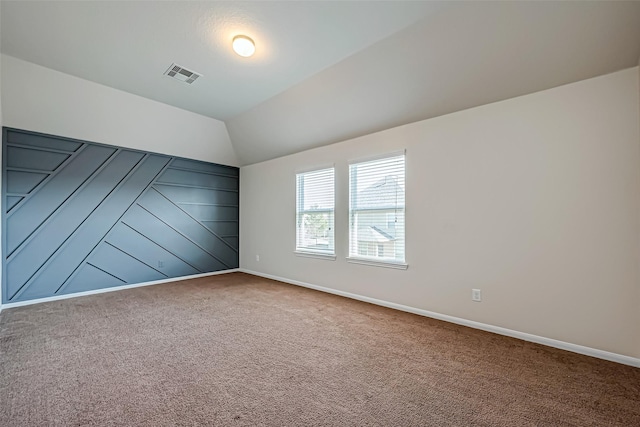 empty room featuring carpet floors, visible vents, vaulted ceiling, and baseboards