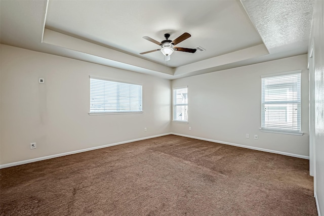 spare room featuring a tray ceiling, carpet flooring, visible vents, and baseboards