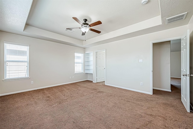 unfurnished bedroom with ceiling fan, carpet flooring, visible vents, baseboards, and a raised ceiling