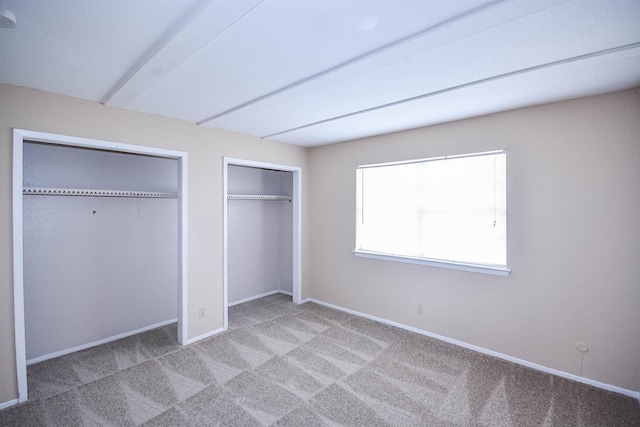 unfurnished bedroom featuring multiple closets and light colored carpet