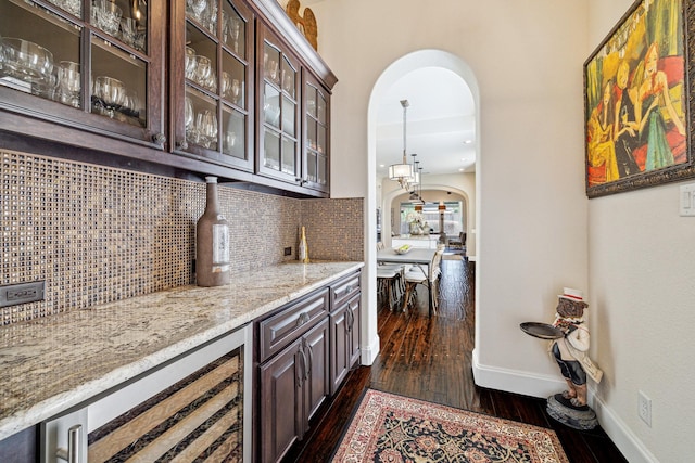 bar with tasteful backsplash, dark hardwood / wood-style flooring, light stone countertops, and dark brown cabinets